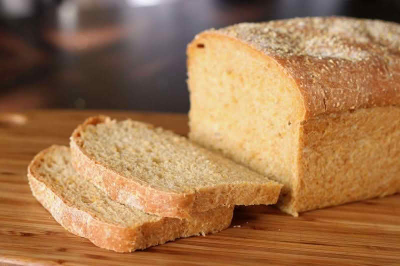 A loaf of anadama bread resting on a wooden cutting board, showcasing its rustic texture and golden-brown crust