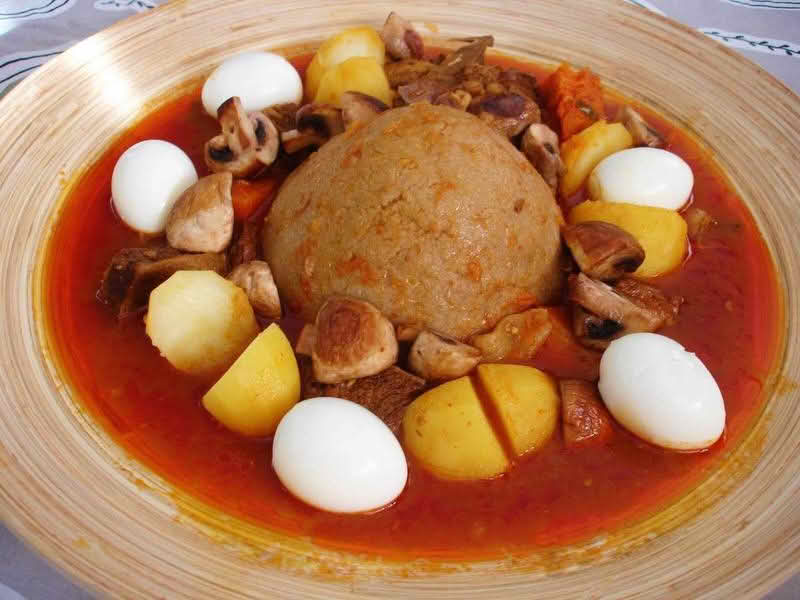A plate of Bazin (center) served with a stew and whole hard-boiled eggs