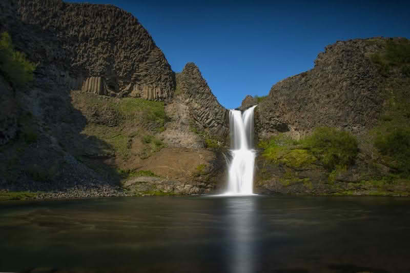 A stunning view of the Selfoss Waterfall cascading into a river, surrounded by natural beauty and rugged terrain