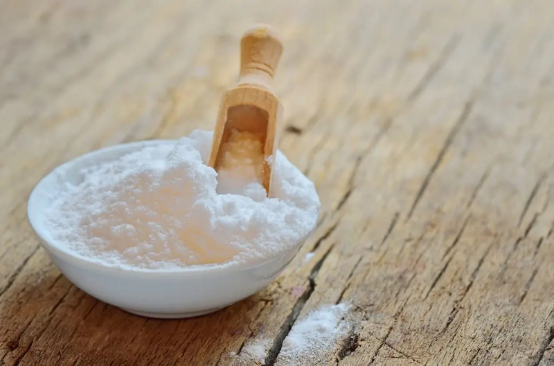 A bowl of baking soda with a wooden spoon resting on top, ready for use in baking or cooking