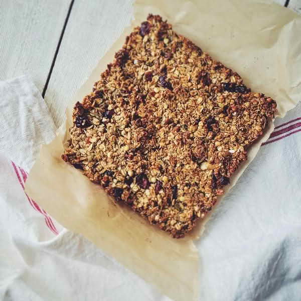High-angle close-up view of a rectangular granola bar resting on a sheet of brown parchment paper, which is itself laid over a white linen cloth with thin red stripes